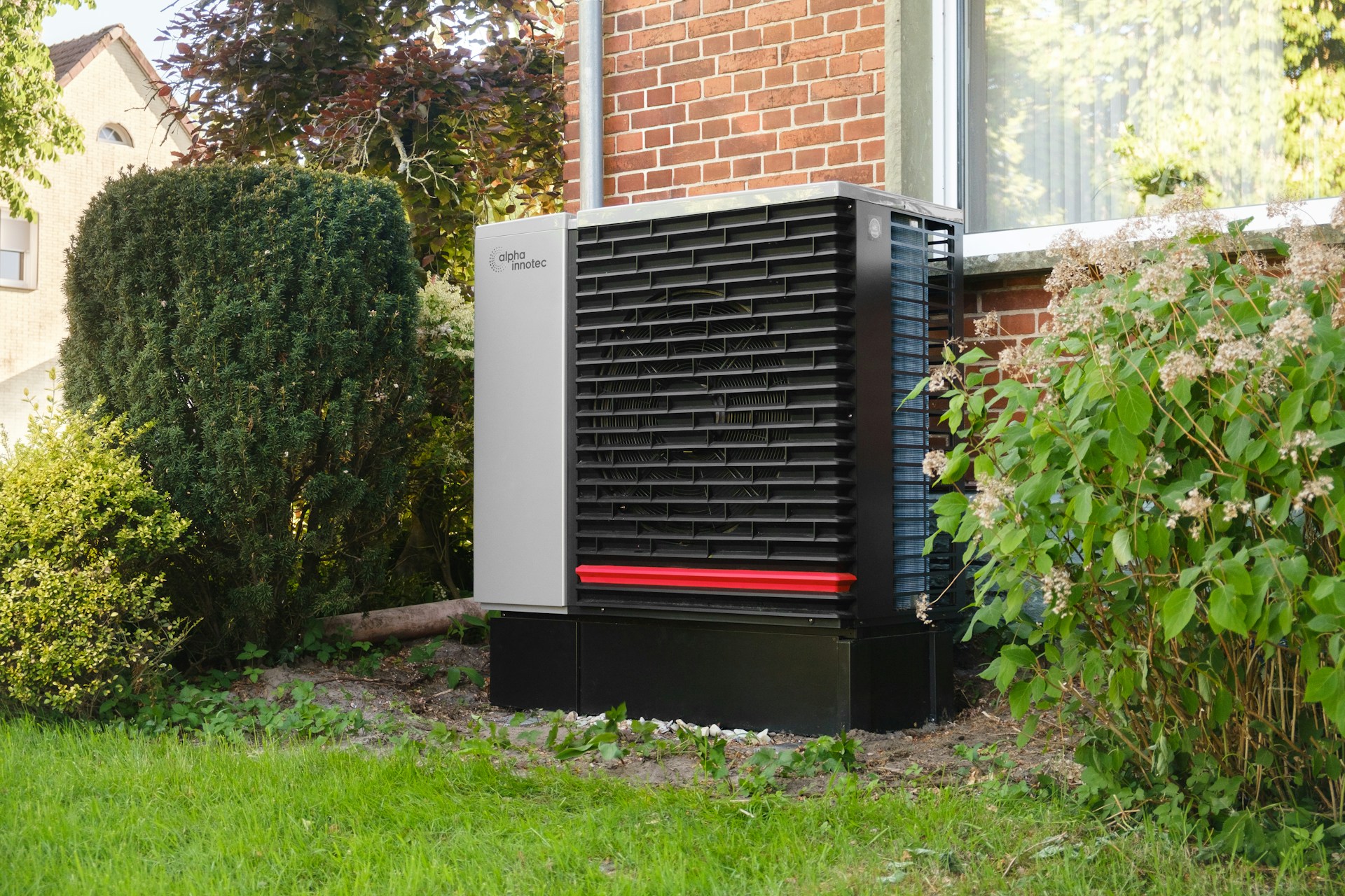 Neat outdoor heat pump unit installed beside a home, screened by garden planting